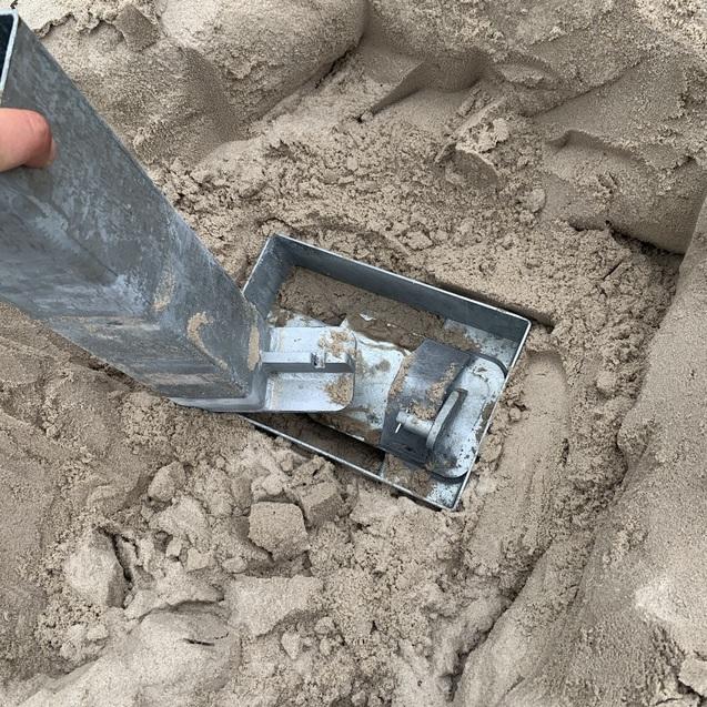 Hand mit Metall-Schaufel, die in weichem Sand einer Grube steckt, umgeben von feinem Sand.