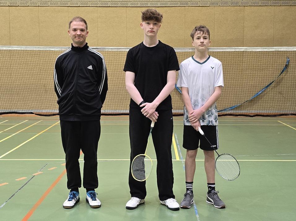 Drei junge M&auml;nner posieren vor einem Badmintonfeld, bereit f&uuml;r das Spiel.