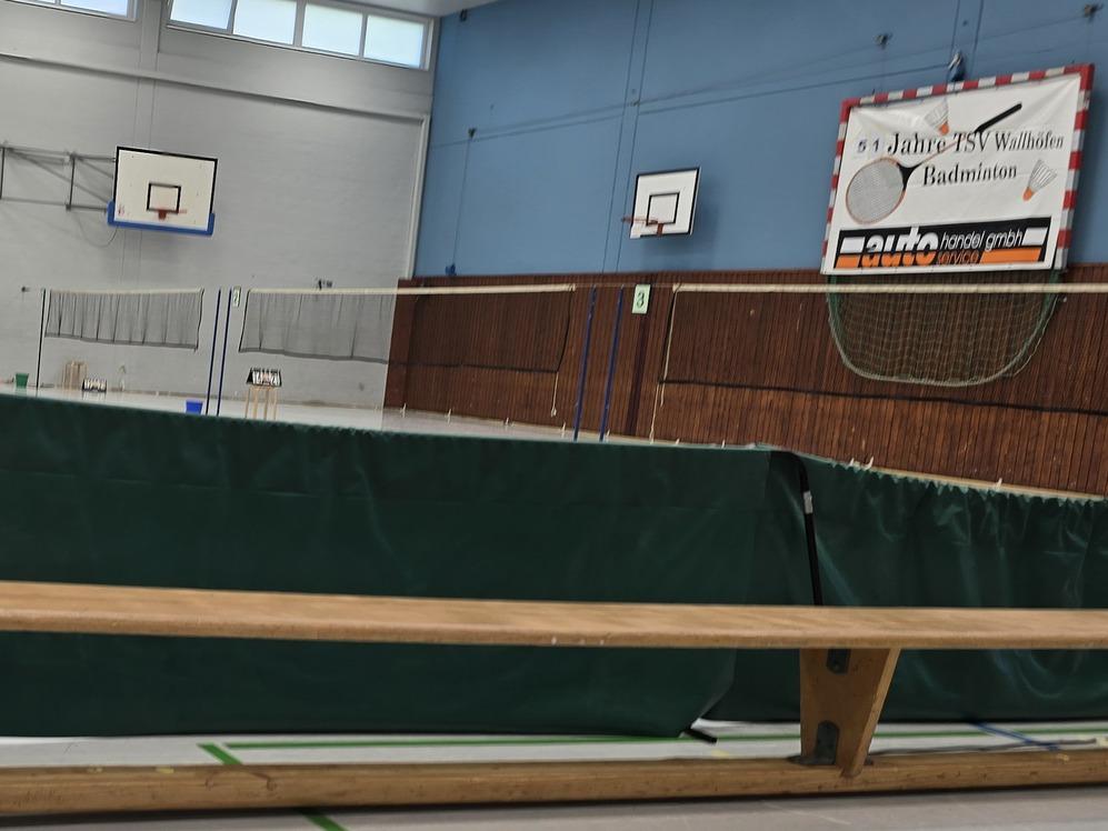 Turnbank und Holzkasten vor einer abgetrennten Sporthalle mit Basketballk&ouml;rben und Badmintonnetz.