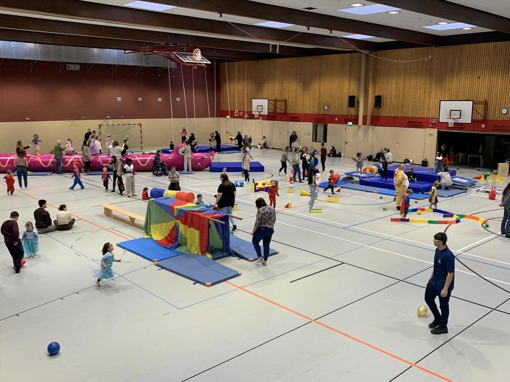 Ein gro&szlig;es Hallensportzentrum mit vielen Menschen, die aktiv an verschiedenen Stationen spielen.