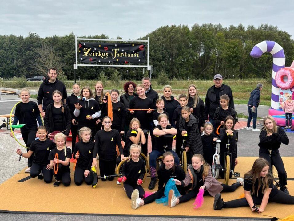 Eine Gruppe von Zirkuskindern in schwarzen T-Shirts lächelt und posiert auf einem Parkplatz nach ihrem Auftritt.