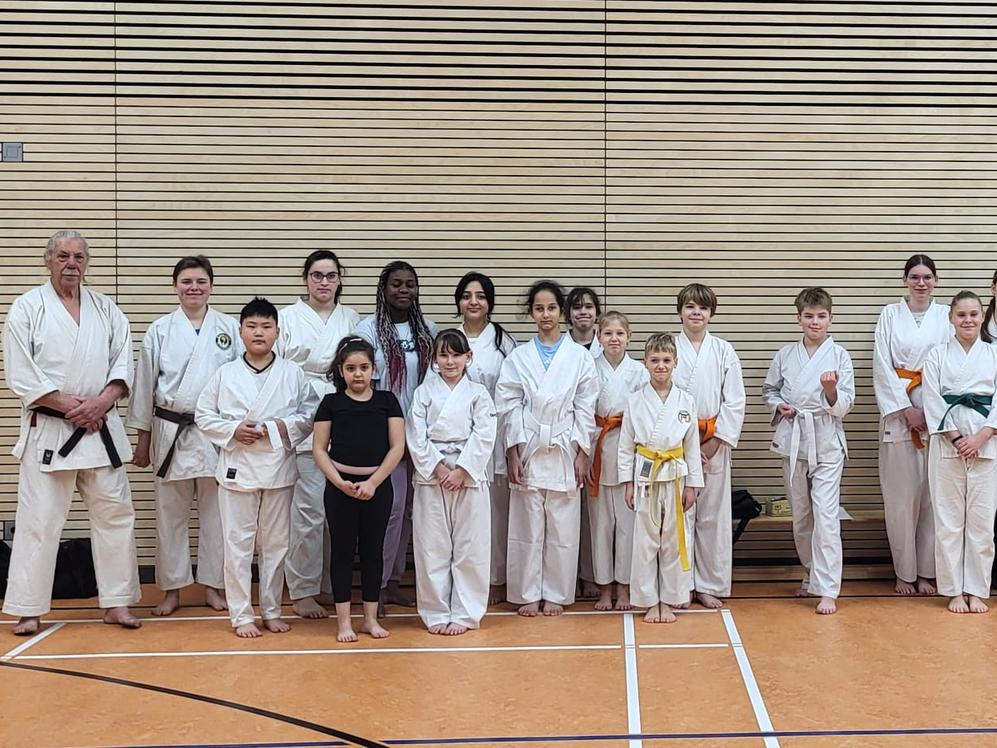 Eine Gruppe von Sportlern l&auml;chelt und posiert in Karateanz&uuml;gen f&uuml;r ein Foto.