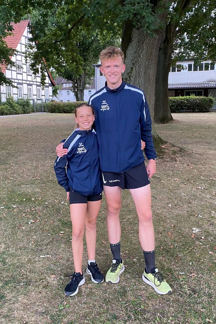 Zwei junge Sportler stehen nebeneinander in Sportkleidung auf einer Wiese, im Hintergrund ein Baum und Gebäude.