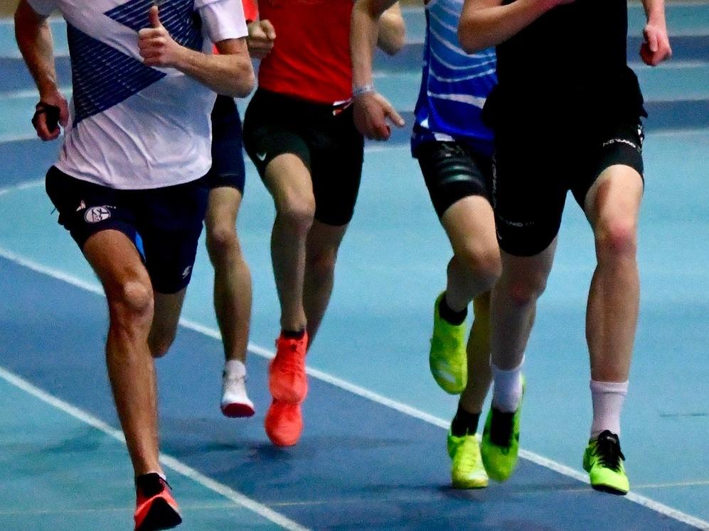 Gruppe von f&uuml;nf L&auml;ufern in sportlicher Kleidung, die auf einer blauen Laufbahn trainieren.
