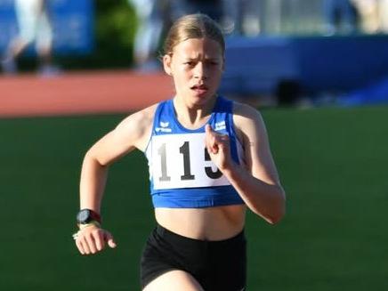 M&auml;dchen in Sportkleidung l&auml;uft auf einer Laufbahn, Nummer 119 auf dem Shirt, im Hintergrund stehen Zuschauer.