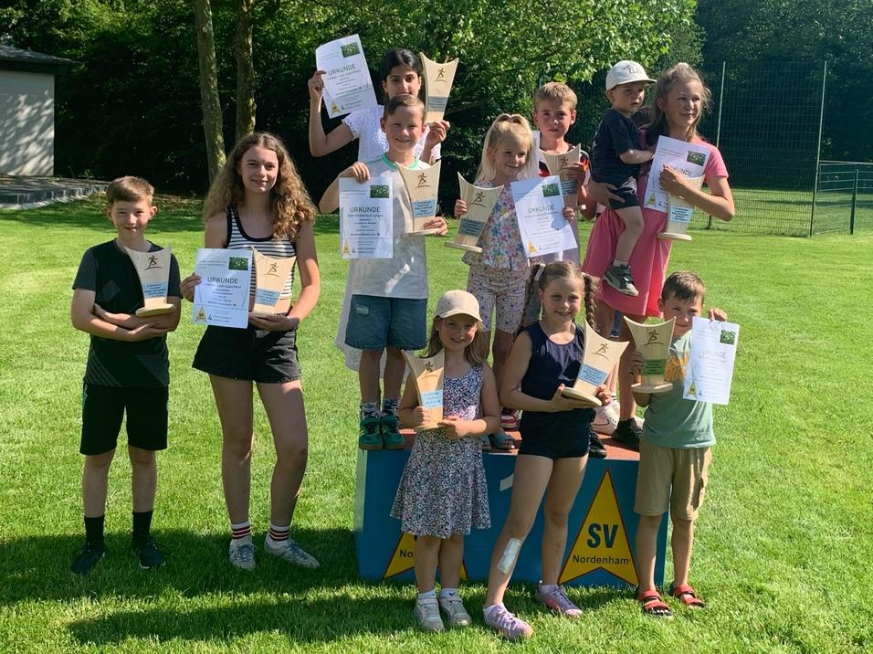 Kinder und Jugendliche stehen mit Urkunden auf und vor einem Siegerpodest auf einer Wiese.