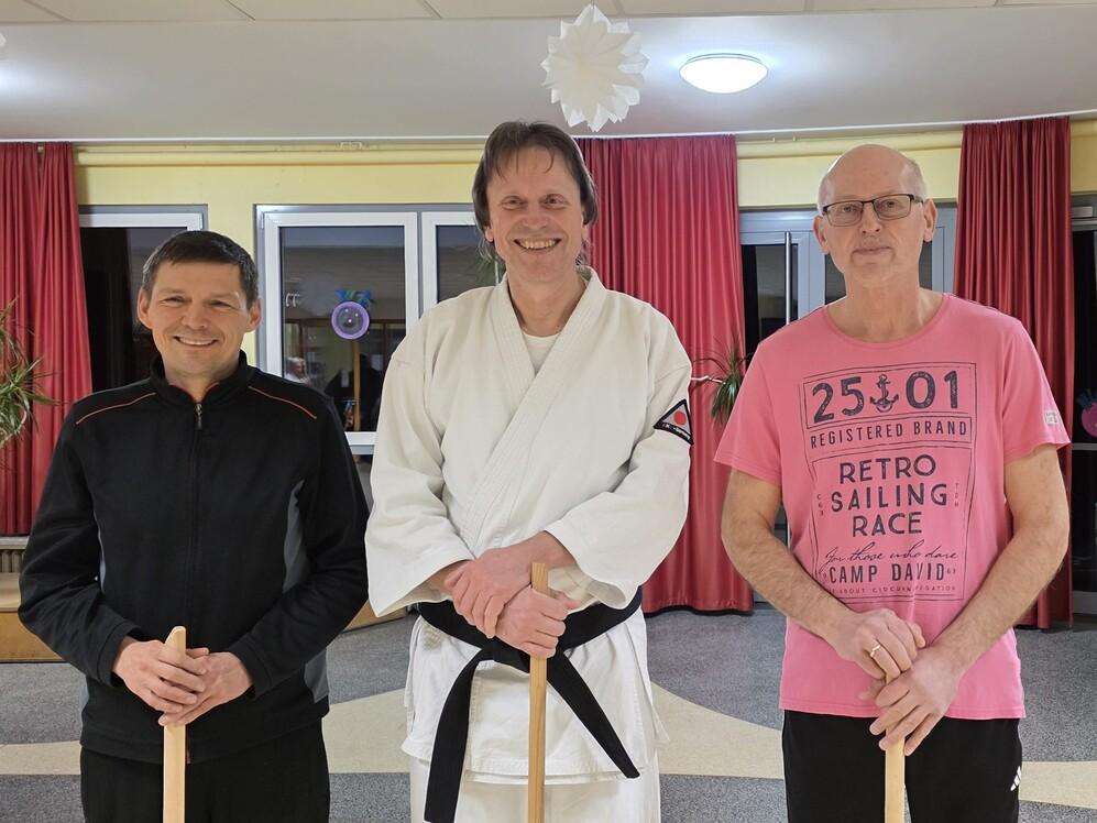 Drei M&auml;nner in Karateanz&uuml;gen posieren l&auml;chelnd f&uuml;r ein Foto.