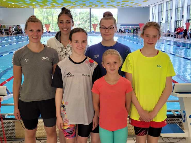 Gruppenfoto von sechs Schwimmerinnen in Sportbekleidung vor einem Schwimmbecken mit blauer Wasseroberfl&auml;che.