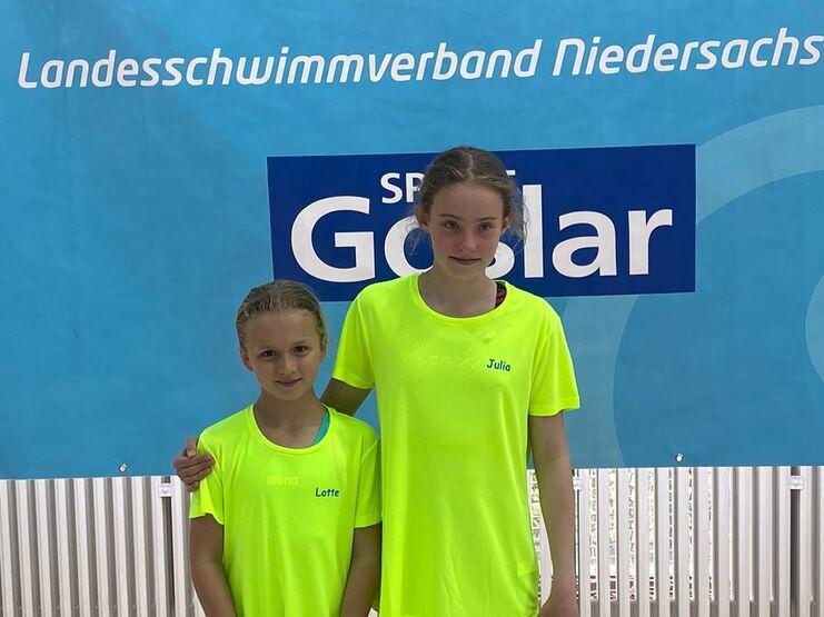 Zwei M&auml;dchen in neonfarbigen Schwimm-T-Shirts stehen vor einem Banner des Landesschwimmverbands Niedersachsen.