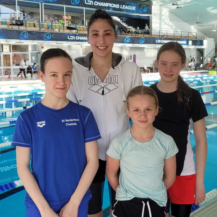 Vier Schwimmerinnen posieren am Beckenrand eines Schwimmbeckens bei einem Wettkampf.