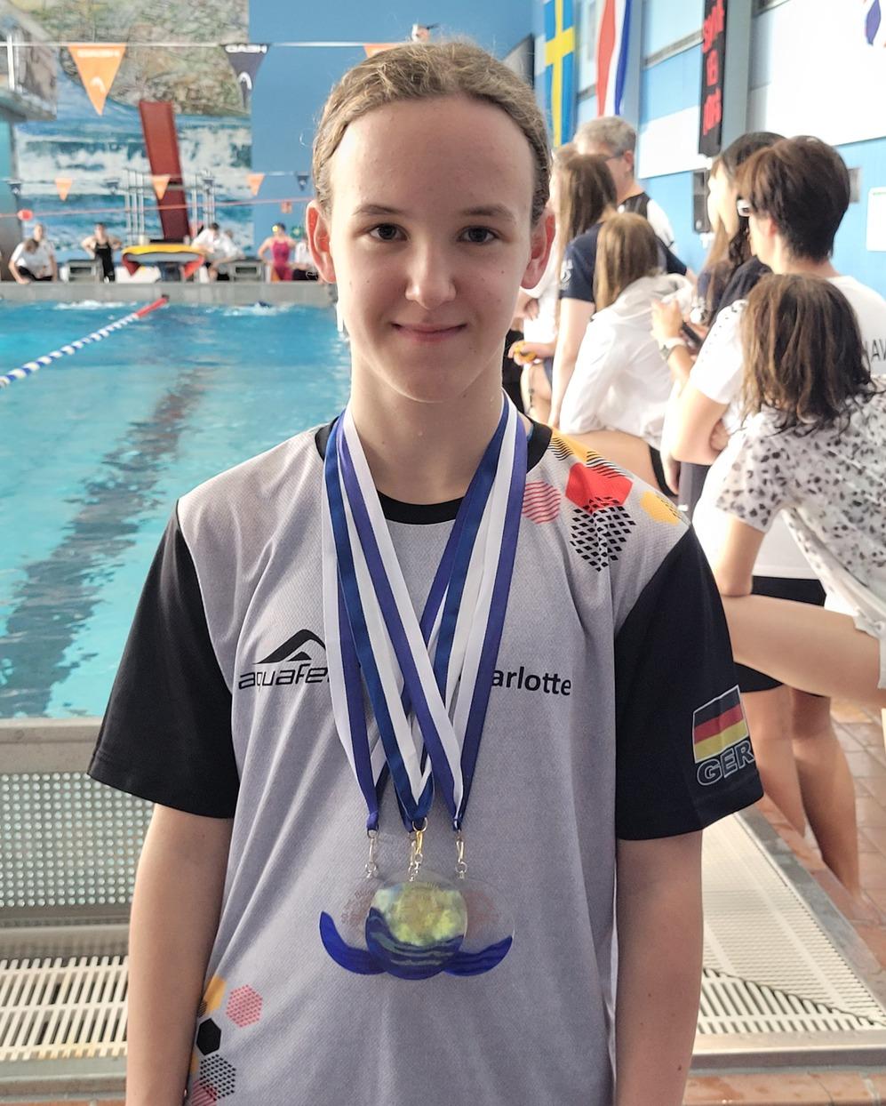 M&auml;dchen in Schwimmkleidung mit Medaillen um den Hals, im Hintergrund ein Schwimmbecken und Zuschauer.