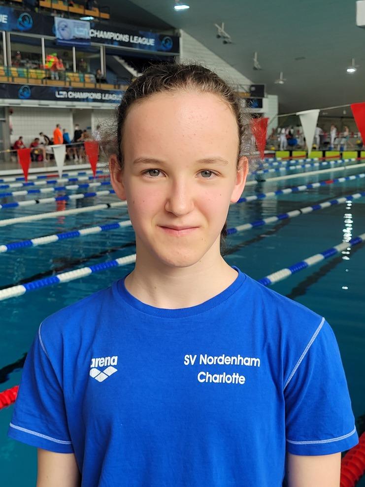 M&auml;dchen in blauer Schwimmetrik mit dem Schriftzug "SV Nordenham" vor einem Wettkampfbecken mit Schwimmbahnen.