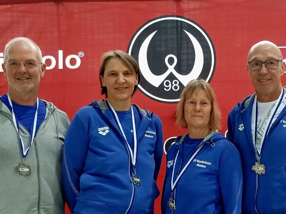 Drei Menschen in blauen Jacken stehen zusammen und schauen freundlich in die Kamera.