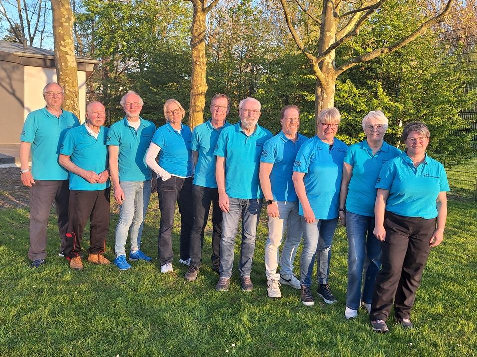 Gruppenshot von zehn Personen in blauen Oberteilen vor einem Schild des Sportvereins Nordenham e.V. im Freien.