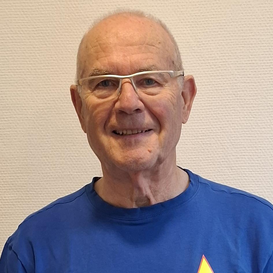 Porträt eines lächelnden Mannes mit Brille in einem blauen T-Shirt. Im Hintergrund eine helle, einfarbige Wand.