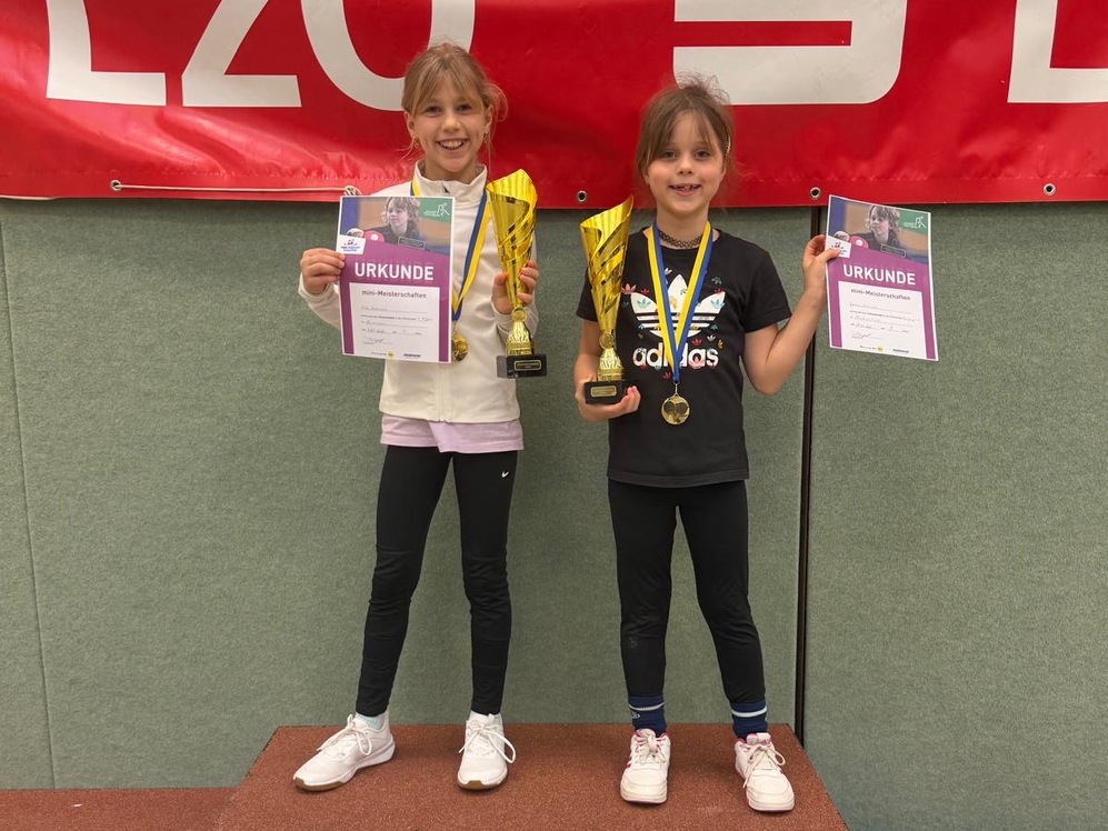 Zwei junge Siegerinnen der Tischtennis-Mini-Meisterschaften pr&auml;sentieren ihren Pokal auf dem Podest in der Sporthalle.