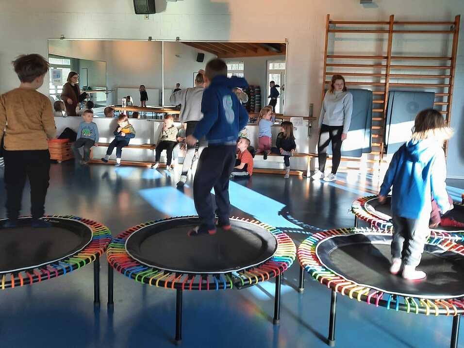Kinder springen auf Mini-Trampolinen in einem hellen Raum, während Erwachsene zuschauen und die Atmosphäre genießen.