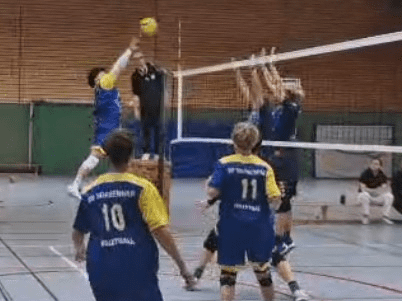 Volleyballspieler in blau-gelben Trikots in Aktion auf dem Spielfeld, w&auml;hrend sie einen Ball &uuml;ber das Netz schlagen.