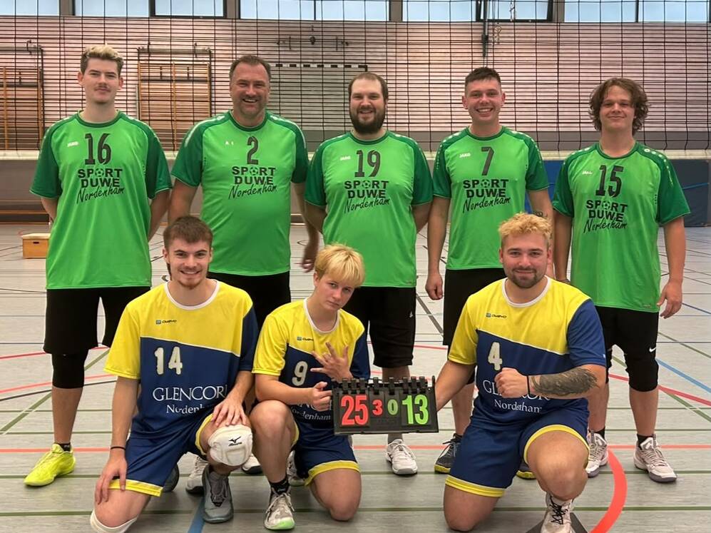 F&uuml;nf M&auml;nner in gr&uuml;nen Trikots und drei M&auml;nner in gelb-blauen Trikots posieren in einer Sporthalle, zwei knien und halten eine Anzeigetafel mit der Zahl '25:13'.