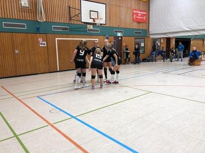 Vier Volleyballspielerinnen in Schwarz versammeln sich auf dem Platz und besprechen sich vor einem Spiel.