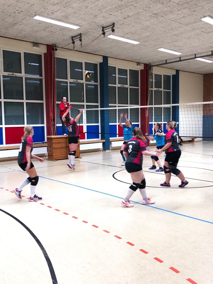 Volleyballtraining mit mehreren Spielerinnen in der Sporthalle, eine Spielerin springt für einen Angriff.