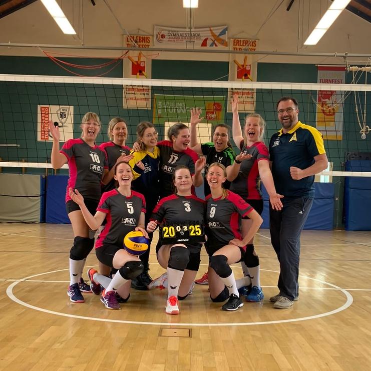 Gruppenselfie eines Volleyballteams auf dem Spielfeld, lächelnd mit einem Scoreboard, das 20:25 zeigt.
