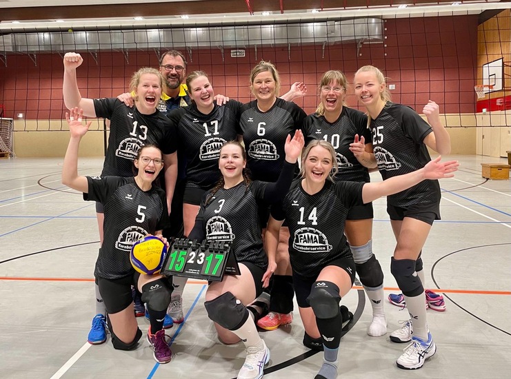 Teamfoto einer weiblichen Volleyballmannschaft in schwarzen Trikots, die nach einem Sieg jubelt und das Ergebnis zeigt.