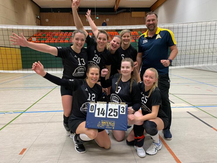 Gruppe von sieben Volleyballspielerinnen und einem Trainer posiert vor einem Netz, alle l&auml;cheln und zeigen den Spielstand 0:25.