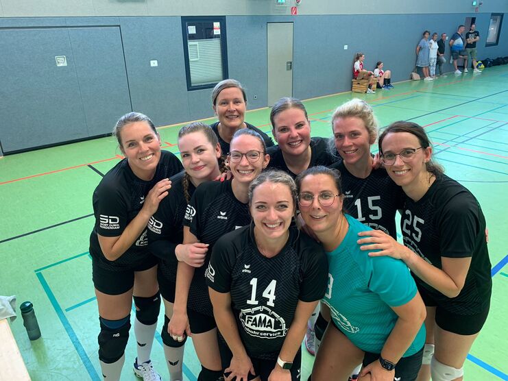 Gruppe von neun Frauen im Sportoutfit stehen l&auml;chelnd auf einem gr&uuml;nen Volley- oder Hallenboden.