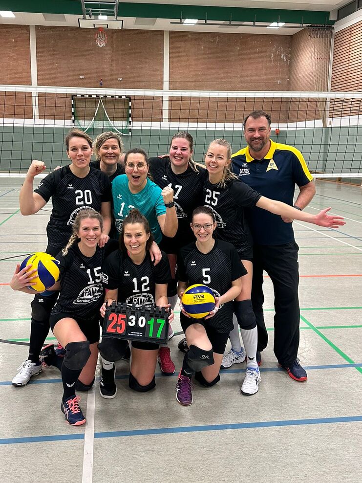 Gruppenselfie einer Volleyballmannschaft mit Spielerinnen in Schwarz, einem Trainer und dem Spielstand 25:17.