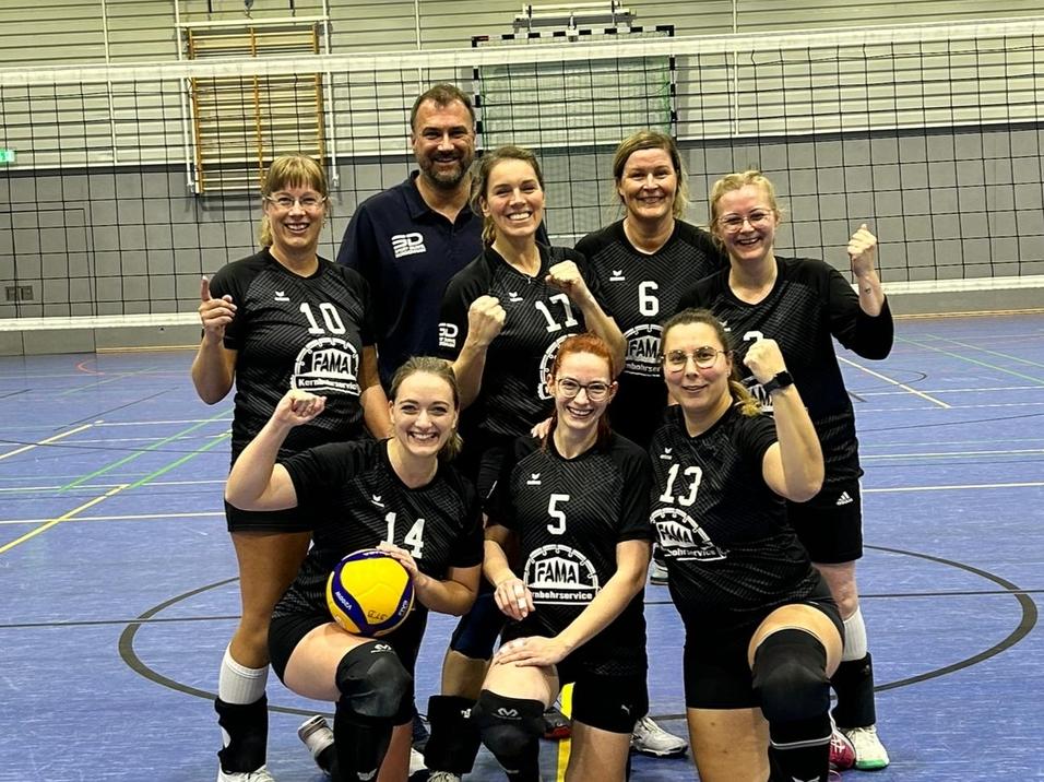 Gruppe von sieben Volleyballspielerinnen in schwarzen Trikots posiert mit einem Volleyball und Punktestand auf dem Feld.