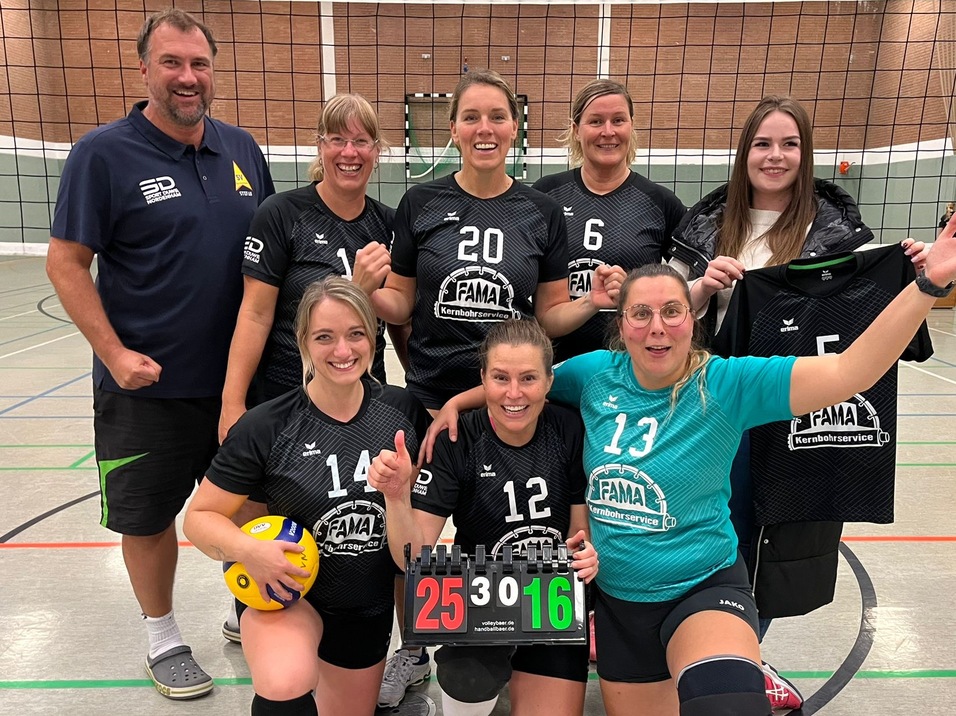Gruppenfoto einer Volleyballmannschaft mit Damen in schwarzen Trikots und Trainer, die einen Sieg pr&auml;sentieren.