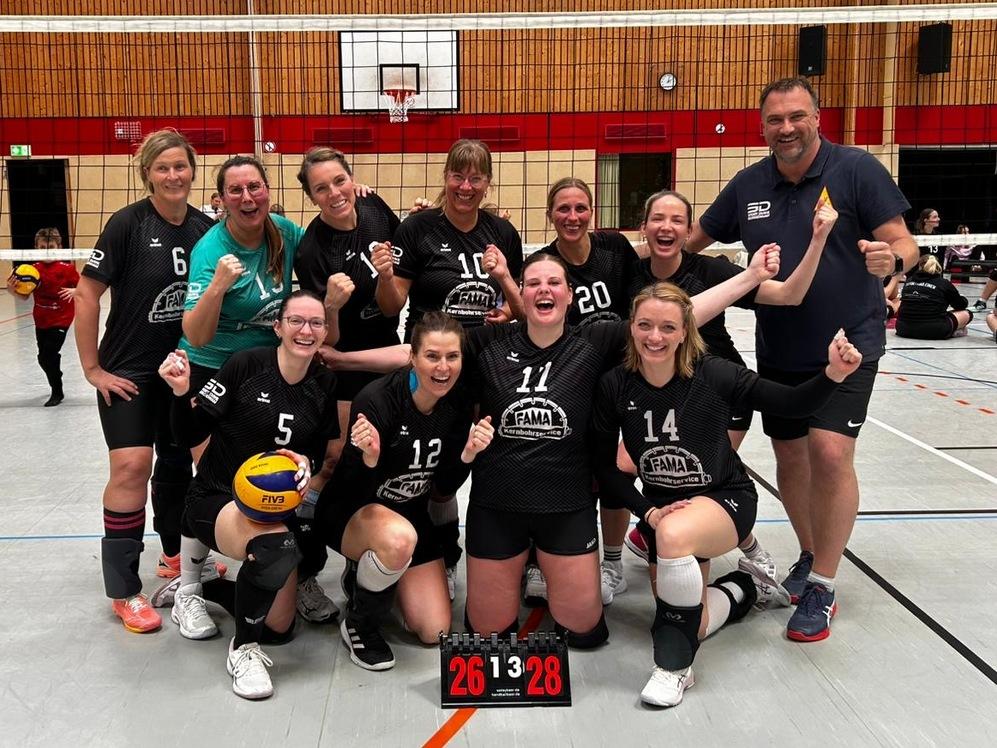 Gruppe von Volleyballspielern in Sportkleidung posiert in einer Halle vor einem Volleyballnetz und einem Basketballkorb.
