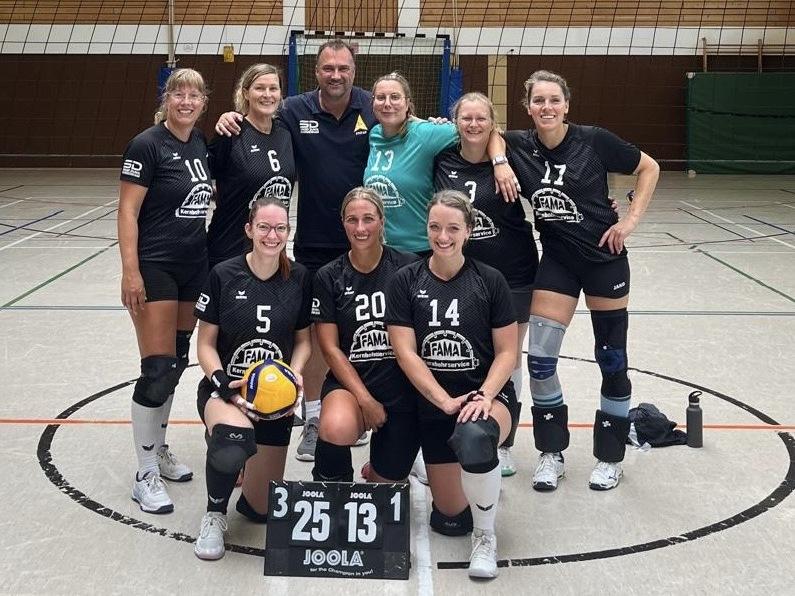 Volleyballspielerinnen posieren in der Sportanlage für ein Gruppenfoto, ausgestattet mit Trikots und Volleyball