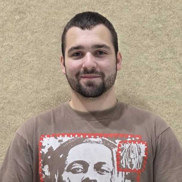 Junger Mann mit Kurzhaarschnitt, tr&auml;gt ein T-Shirt mit Aufdruck, h&auml;lt einen Ball in beiden H&auml;nden.