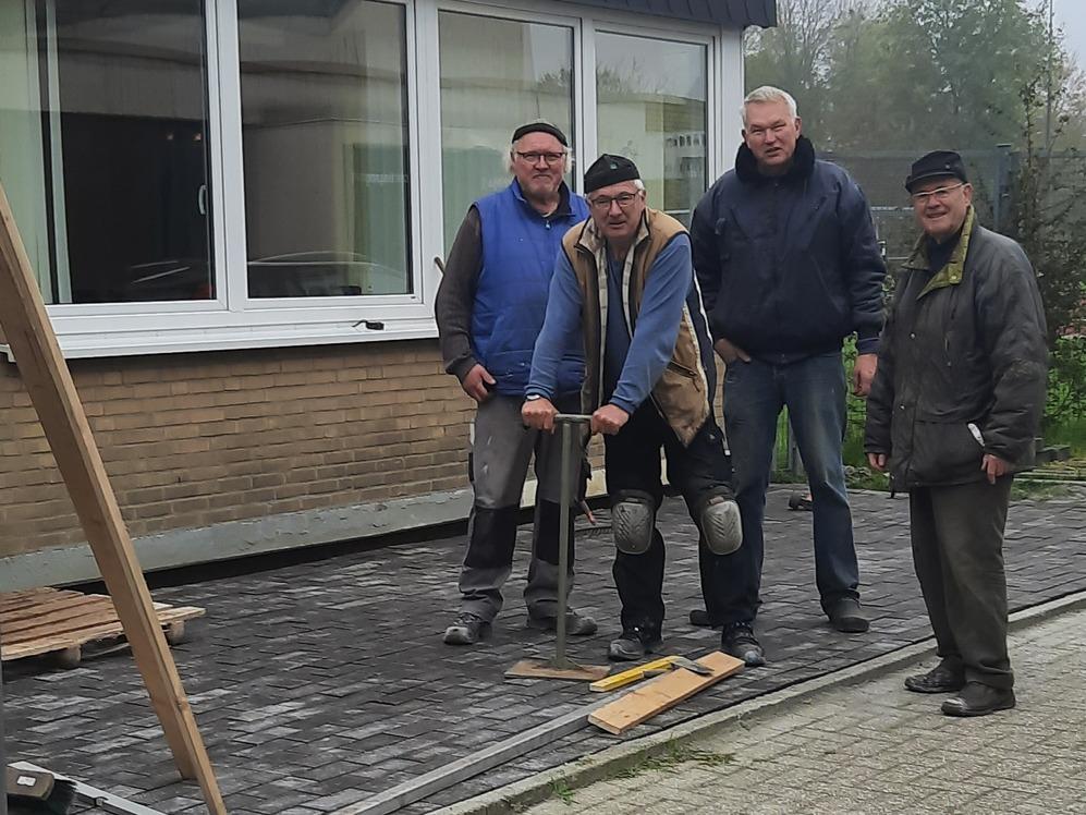 Vier Männer stehen vor einem Gebäude, während sie an einem Bauprojekt mit Steinen und Werkzeug arbeiten.