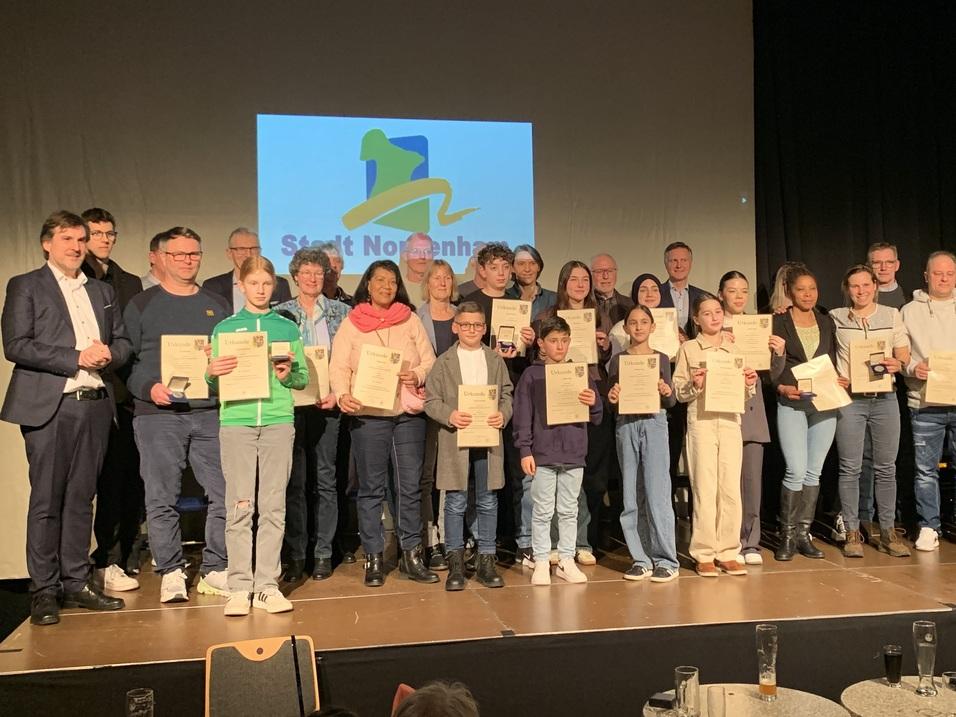 Gruppennfoto von 20 Personen mit Urkunden auf einer Bühne, hinter ihnen das Logo der Stadt Nordhausen.