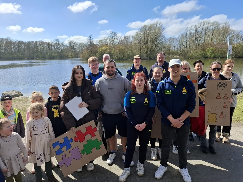 Vor einem See posiert eine Gruppe von Personen mit verschiedenen Puzzlest&uuml;cken in der Hand.