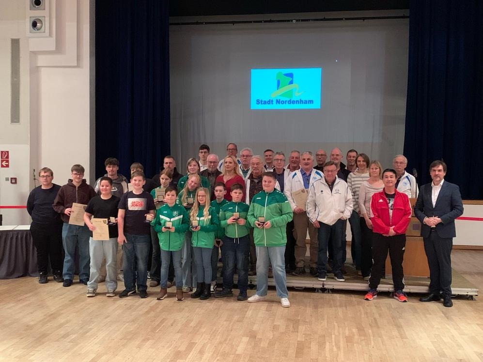 Sportler:innen posieren vor der B&uuml;hne w&auml;hrend der Sportlerehrung in der Stadthalle Friedeburg.