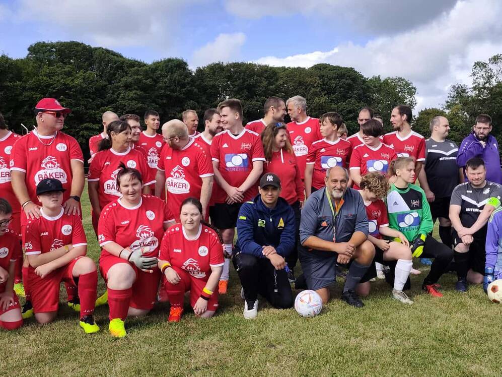 Gruppe von Fu&szlig;ballspielern in roten und dunklen Trikots steht und kniet auf einem Rasenplatz.