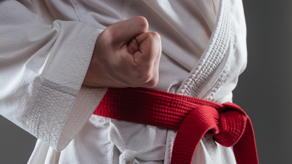 Nahaufnahme einer geballten Faust eines Karateka in einem weißen Gi mit rotem Gürtel.