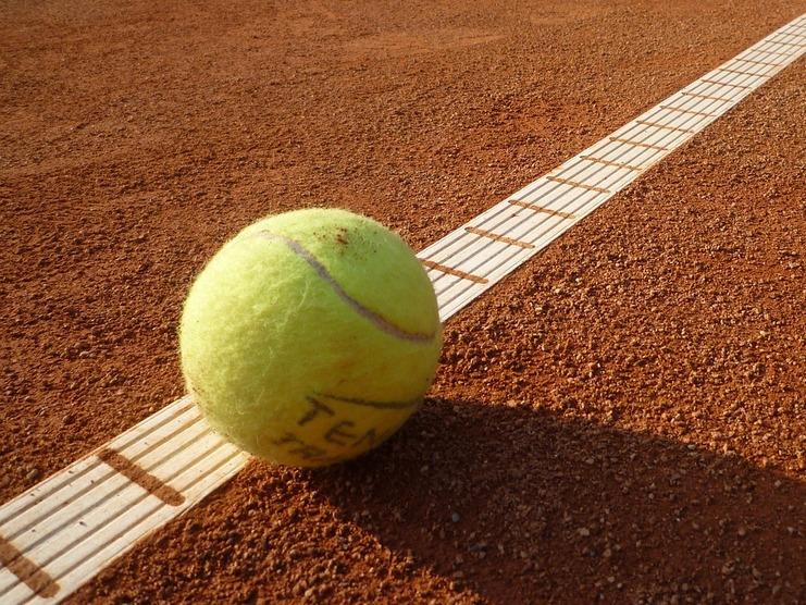 Gelber Tennisball liegt auf einer roten Sandplatzlinie mit weißen Markierungen.